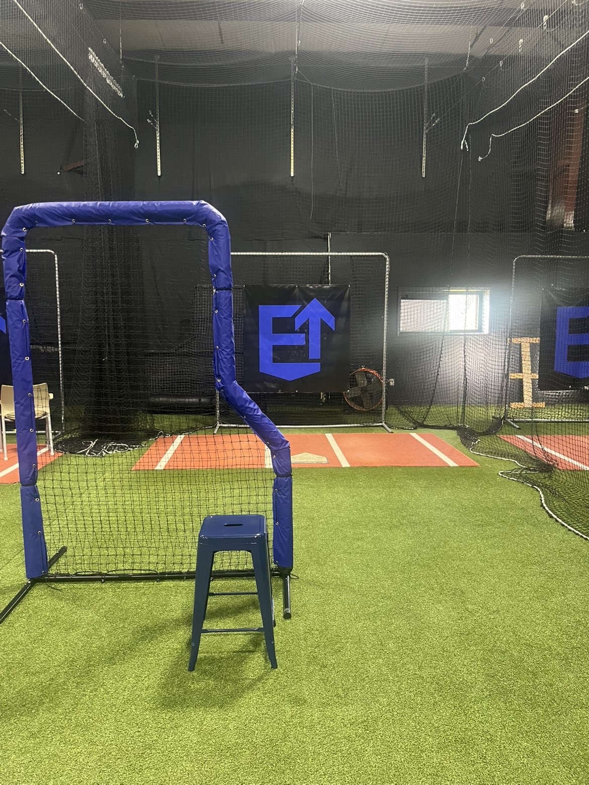 Indoor batting cage with blue L-screen and Elevate logo